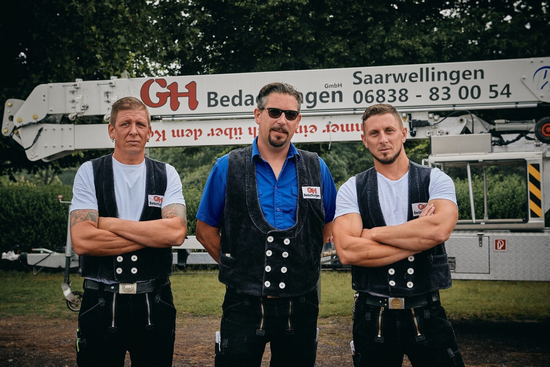 Drei Mitarbeiter in Zunftkleidung vor der Hebebühne